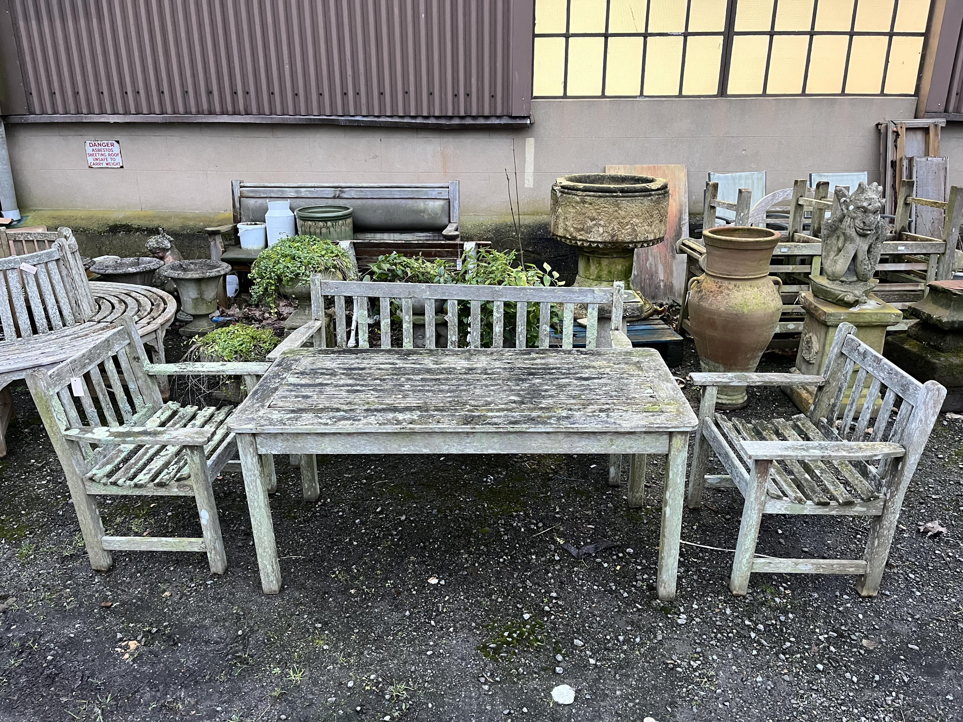 A slatted weathered teak rectangular garden table, width 149cm, depth 70cm, height 68cm, a bench and two armchairs. Condition - fair